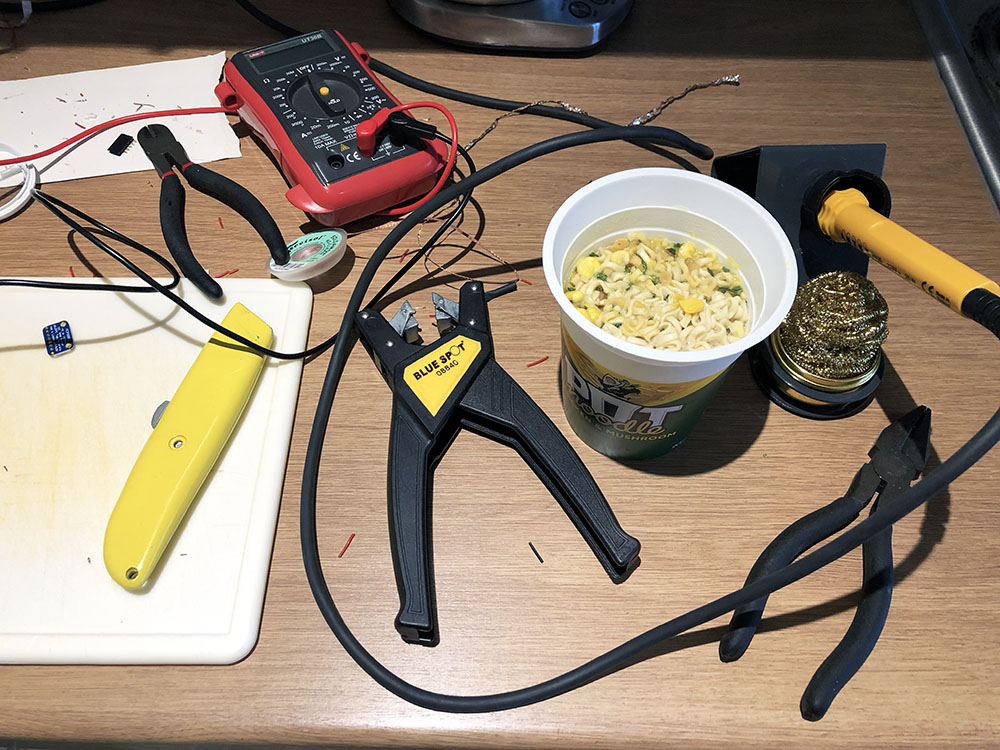 A pot noodle surrounded by tools including a soldering iron, wire cutters and a multi meater.